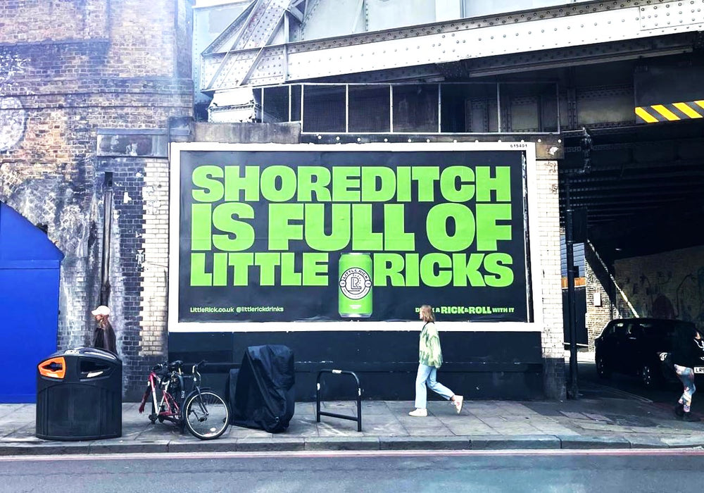A woman walks past a bright green billboard reading Shoreditch is full of little pricks.