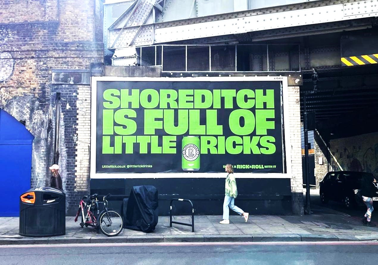 A woman walks past a bright green billboard reading Shoreditch is full of little pricks.