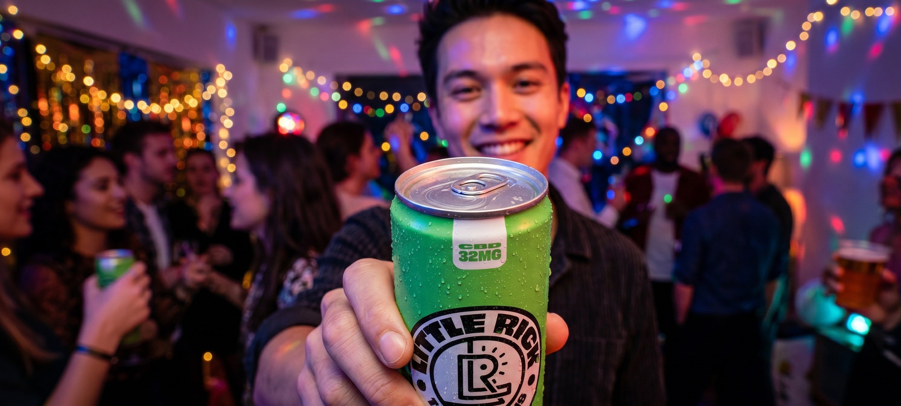 Guy holding a green can at a party, with lights and people in the background.